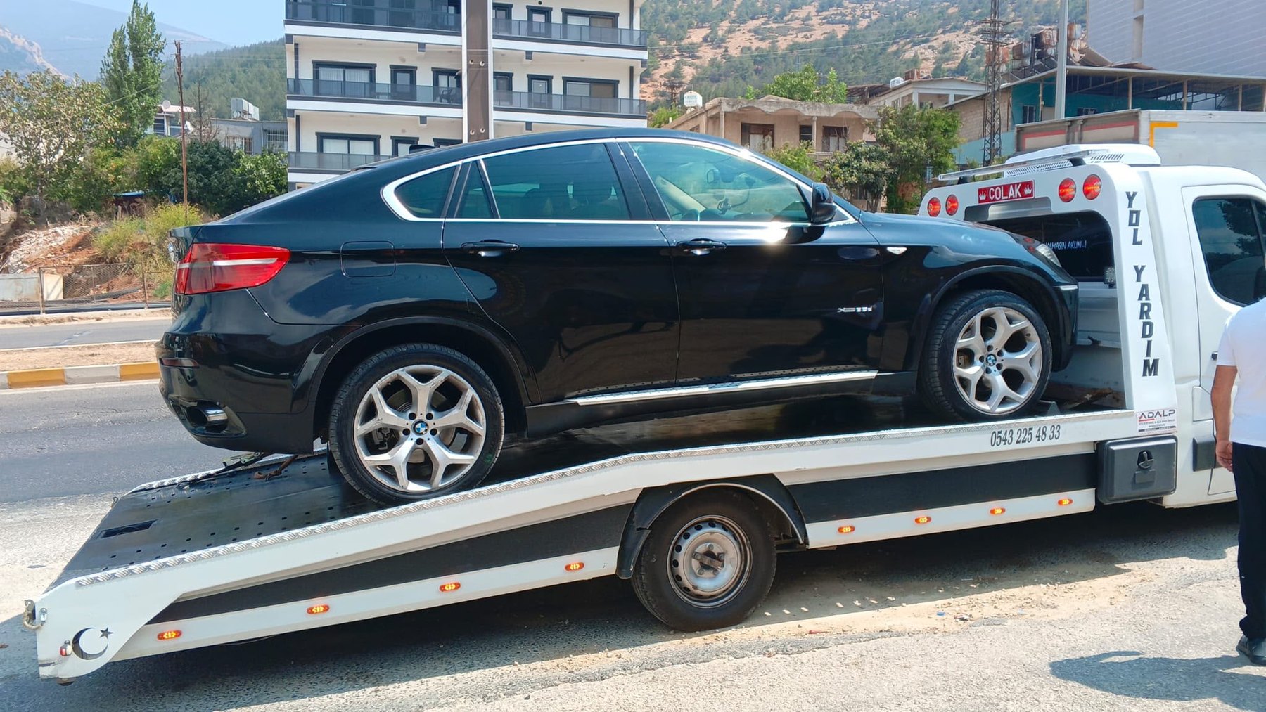 Çolak Oto Kurtarma çekicisinin kasasında taşınan siyah SUV, dağ eteğinde bir caddede